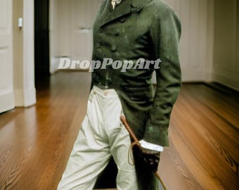 May include: A man wearing a dark green coat with a white cravat and white pants. He is holding a riding crop in his right hand. The background is a wooden floor.