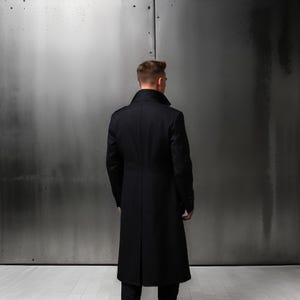 Może przedstawiać: Długi czarny płaszcz z wysokim kołnierzem i zapięciem na guziki.
