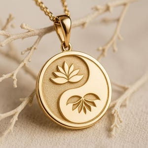 Può includere: Collana con pendente dorato con design Yin e Yang e dettagli di fiori di loto. Il pendente rotondo è appeso a una delicata catena d'oro. Lo sfondo è di un colore morbido e neutro.