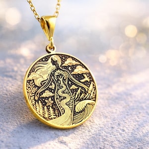 May include: A gold-toned circular pendant necklace featuring an intricate embossed design of a figure integrated with nature elements including a flowing river, a tree, mountains, clouds, stars, and a forest, suspended from a matching gold chain.