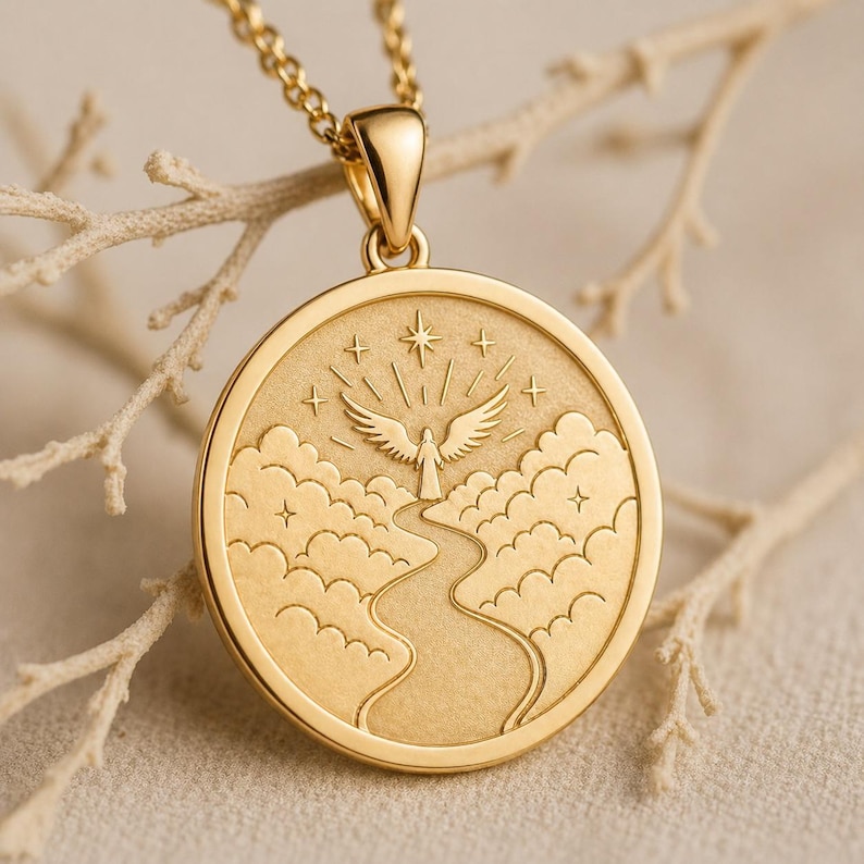 May include: A gold-toned circular pendant necklace featuring an engraved design of a winged figure standing at the end of a winding path through clouds, topped with a large star and smaller stars, suspended from a matching gold-toned chain.
