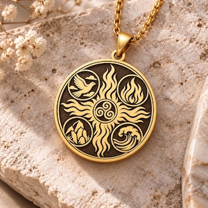 May include: A gold-toned circular pendant necklace featuring a central triskelion symbol surrounded by four distinct circular engravings depicting a bird, flames, mountain peaks, and ocean waves, all set against a dark textured background.
