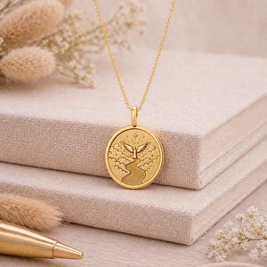May include: A gold-toned necklace featuring a circular pendant with an embossed design of a winged figure standing at the end of a winding path amidst clouds and stars. The pendant hangs from a delicate gold-toned chain with a polished finish.
