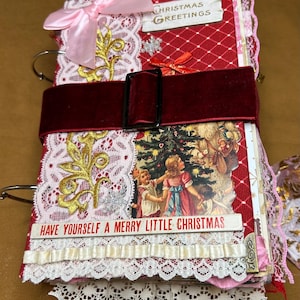 May include: A handmade Christmas journal with a red and white diamond pattern cover, adorned with lace, a pink bow, and a burgundy velvet belt. The journal features the text "Christmas Greetings" and "Have Yourself a Merry Little Christmas."