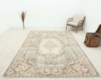 May include: A large, rectangular, vintage-style rug with an intricate floral pattern in shades of beige, gray, and muted green. The rug is centered in a room with a wooden chair, a vintage record player, and a vase with dried plants.