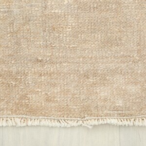 K&ouml;nnte beinhalten: Nahaufnahme eines beigefarbenen Teppichs mit strukturierter Oberfl&auml;che. Der Teppich hat ein gewebtes Muster und einen Fransenbesatz am unteren Rand. Die Farbe ist ein neutrales Beige, passend f&uuml;r verschiedene Einrichtungsstile.