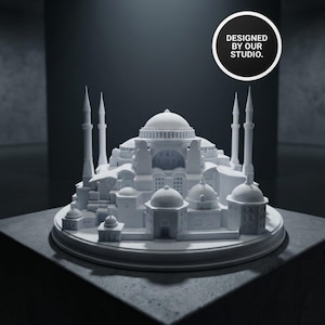 Può includere: Un modello architettonico bianco dettagliato di un edificio con più cupole, minareti e dettagli intricati. Il modello è su una base rotonda e una superficie scura. Il testo "DESIGNED BY OUR STUDIO" è in un cerchio nero.