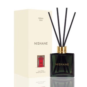 Pode incluir: Um difusor de vidro verde escuro com varetas pretas e uma tampa dourada. A caixa creme atrás tem as palavras "INDIAN OUD" e "NISHANE" impressas. A caixa também apresenta uma ilustração de porta vermelha.