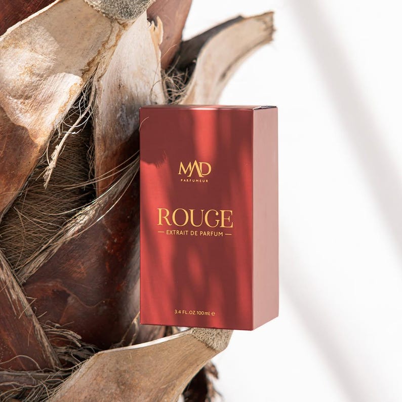 May include: A red perfume box with gold lettering and the text "ROUGE - EXTRAIT DE PARFUM". The box also features the brand logo "MAD PARFUMEUR" and indicates a volume of 3.4 fl oz (100ml).