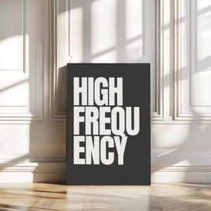 Puede incluir: Una impresión enmarcada en negro con las palabras "HIGH FREQUENCY" en letras mayúsculas blancas y en negrita. La impresión se muestra contra una pared blanca con molduras y un suelo de madera.