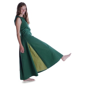 Könnte beinhalten: Eine Frau trägt ein grünes und gelbes Kleid mit einem langen Rock. Der Rock ist an den Seiten geteilt und hat auf jeder Seite ein gelbes Panel.