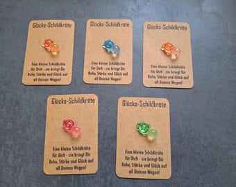 May include: Five small, colorful turtle charms on brown cards with the text "Glücks-Schildkröte" and a message in German about good luck and happiness.