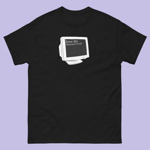 Puede incluir: Camiseta negra con un gráfico blanco de un monitor de ordenador antiguo. El monitor muestra el texto "Error 404 Motivation Not Found". La camiseta está hecha de un material suave y tiene mangas cortas.