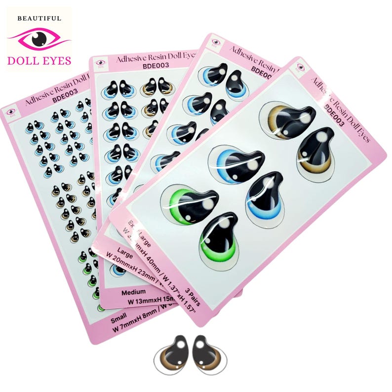 May include: Three sheets of adhesive resin doll eyes in various sizes. The sheets are pink with white borders and feature different colored eyes. The text on the sheets reads "Adhesive Resin Doll Eye" and "BDE003".
