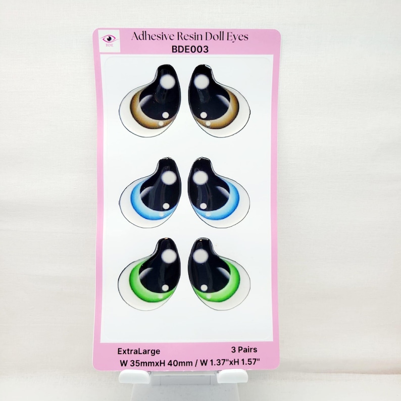 May include: Three pairs of extra-large adhesive resin doll eyes. The eyes are brown, blue, and green. Each pair is 1.37 inches wide and 1.57 inches tall.