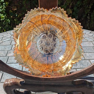 May include: A vintage amber glass bowl with a scalloped edge and intricate cut glass design. The bowl is displayed on a wooden stand.