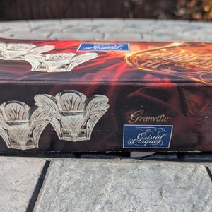 May include: A rectangular box with a dark red and gold design featuring images of crystal candle holders and a French horn. The box is labeled "Granville" and "Cristal d'Arques". The box has a 24% label.