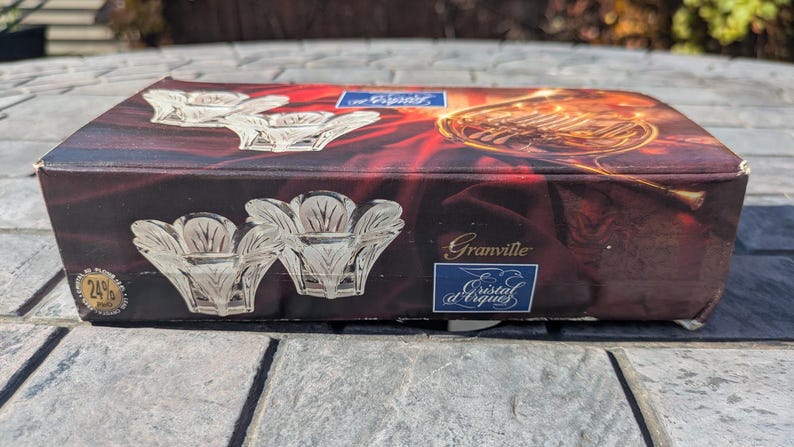 May include: A rectangular box with a dark red and gold design featuring images of crystal candle holders and a French horn. The box is labeled "Granville" and "Cristal d'Arques". The box has a 24% label.