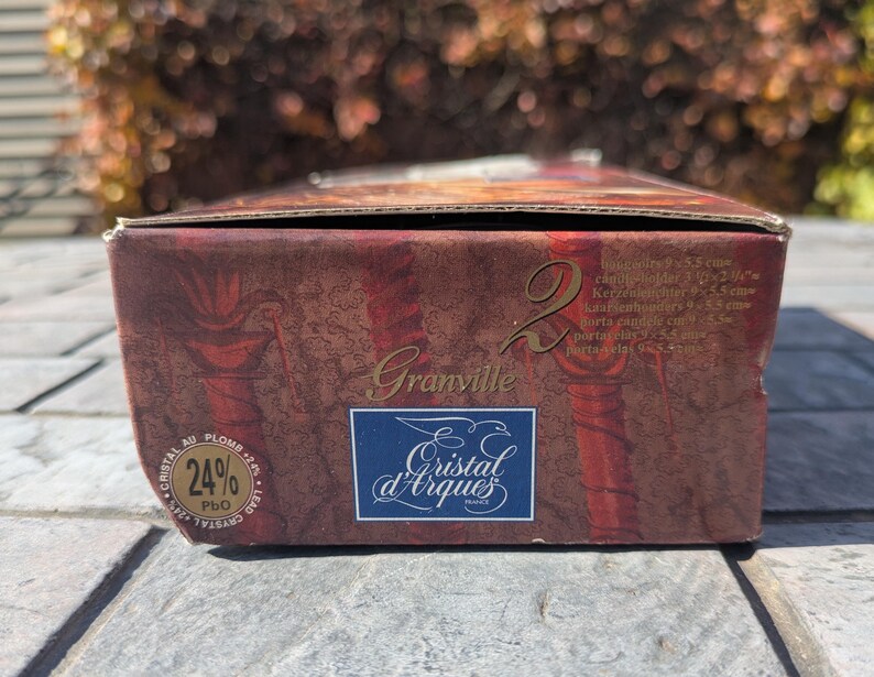 May include: A rectangular box with a burgundy and gold design. The box features the text "Granville" and the logo "Cristal d'Arques France". The box also has text indicating the contents are candle holders, with dimensions of 3.75 x 2.125 inches.