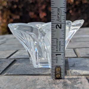 May include: A clear, decorative glass bowl with a flared, petal-like design. The bowl is approximately 2 inches tall, as measured by a ruler. The bowl's sides have a textured, etched pattern. The bowl is sitting on a gray, textured surface.
