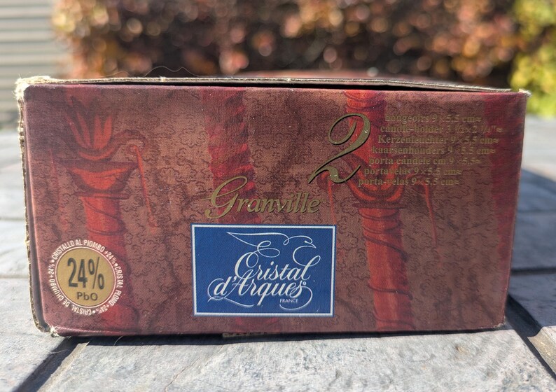 May include: A maroon box with gold lettering that reads "Granville" and the number "2". The box features the "Cristal d'Arques France" logo and a label indicating 24% PbO. The box also lists candle holder dimensions.