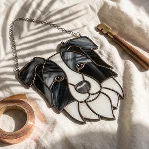 May include: Stained glass dog head with black, white, and gray sections, hanging from a silver chain. A copper tape roll and a glass cutter with a wooden handle are also visible.