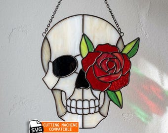 Könnte beinhalten: Ein Buntglas-Sonnenfänger in Form eines Schädels mit cremefarbenem Schädel, schwarzen Augen- und Nasenhöhlen sowie einer leuchtend roten Rose mit grünen Blättern über einem Auge. Das Stück hängt an einer schwarzen Kette und trägt das Etikett SVG CUTTING MACHINE COMPATIBLE.