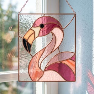 May include: A rectangular stained glass suncatcher featuring a flamingo design. The piece is crafted with various shades of pink, coral, and white glass, accented by a black eye and beak tip, all held together by copper-toned metal solder lines.