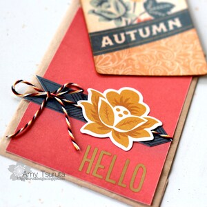 May include: A red card with the word "HELLO" in gold letters, a yellow flower with brown accents, and a black and white striped twine bow. The card is layered on top of a brown card with a tag that says "AUTUMN" in black letters.