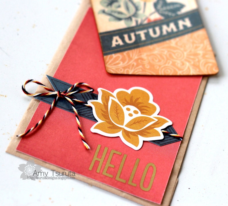 May include: A red card with the word "HELLO" in gold letters, a yellow flower with brown accents, and a black and white striped twine bow. The card is layered on top of a brown card with a tag that says "AUTUMN" in black letters.