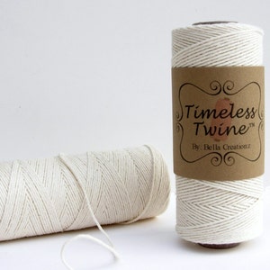 May include: Two spools of natural white cotton twine. The twine is wound around cardboard spools with brown paper labels. The label on the spool in the foreground reads "Timeless Twine&trade; By: Bella Creations."