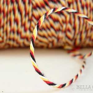 May include: A close-up of a spool of black, white, red, and yellow twine. The twine is twisted together in a rope-like pattern.