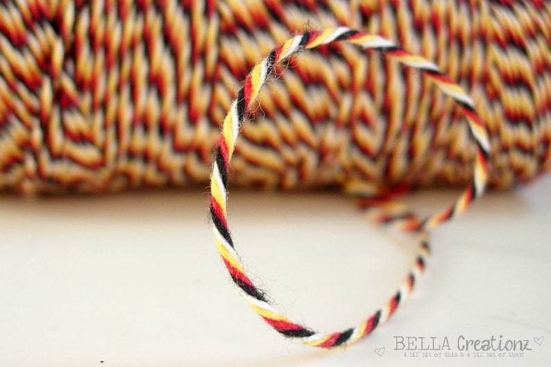 May include: A close-up of a spool of black, white, red, and yellow twine. The twine is twisted together in a rope-like pattern.