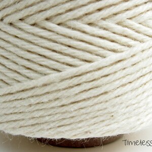 May include: A close-up of a spool of natural white cotton twine. The twine is tightly wound and has a smooth, even texture. The spool is labeled "Timeless Twine".