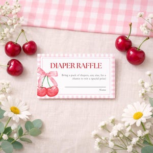 May include: A pink and white gingham-patterned diaper raffle card with the text "DIAPER RAFFLE". The card features a watercolor illustration of cherries and a pink bow. Fresh cherries and daisies surround the card.