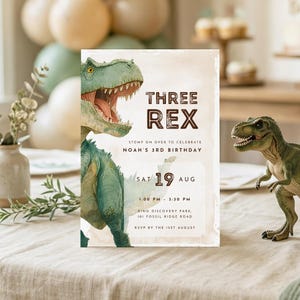 May include: A birthday party invitation with a dinosaur theme. The invitation features a green Tyrannosaurus Rex illustration and the text "THREE REX" with event details. A toy dinosaur is on the table.