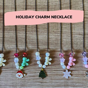 May include: A set of seven holiday charm necklaces with various Christmas-themed charms, including a reindeer, Santa Claus, a Christmas tree, a snowflake, and a bow. The necklaces are made with black chains and white beads.