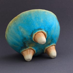 May include: A turquoise blue ceramic bowl with three legs. The bowl has a mottled glaze and a slightly irregular shape.
