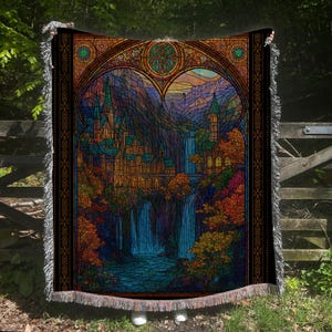 Può includere: Una coperta nera con un disegno a vetrata raffigurante un castello, cascate e montagne. L'opera d'arte è incorniciata da un bordo decorativo e ha bordi sfrangiati. La tavolozza dei colori comprende sfumature di blu, arancione e verde.