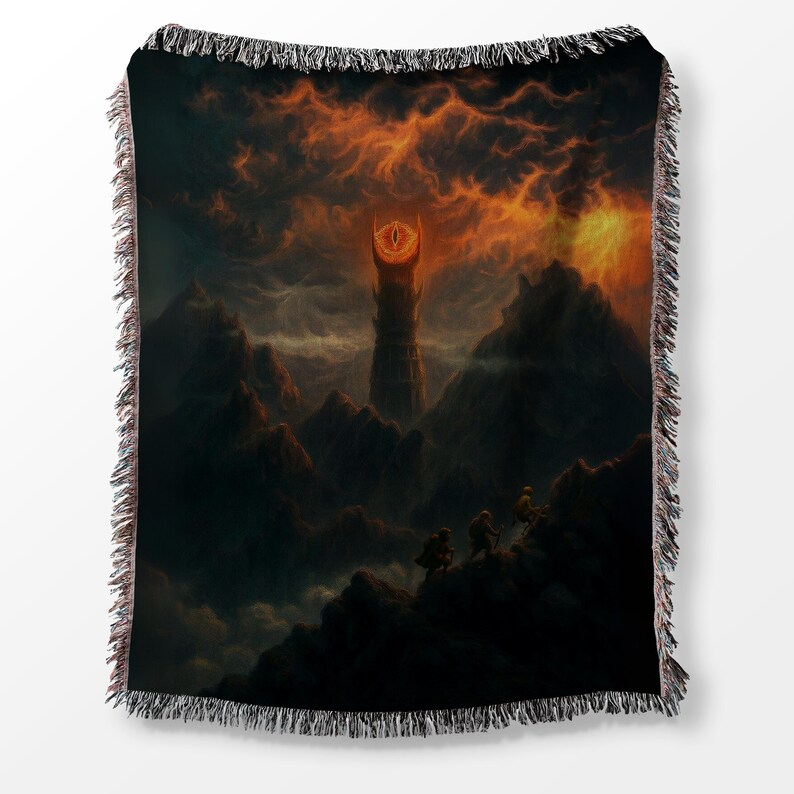 Puede incluir: Manta tejida con un paisaje de fantas&iacute;a que presenta una alta torre y un ojo ominoso en el cielo. La obra de arte representa un terreno monta&ntilde;oso oscuro bajo un cielo naranja ardiente, con figuras en primer plano.