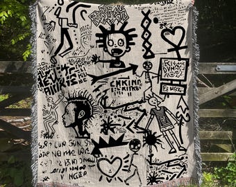 Puede incluir: Manta tejida en blanco y negro con un diseño gráfico que presenta figuras abstractas, corazones, flechas y texto, incluyendo "CHKING" y "LEKIVUSPJE DVM".