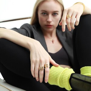 Woman wearing chunky gold rings with a sleek design, styled with gold hoop earrings and a matching bracelet.