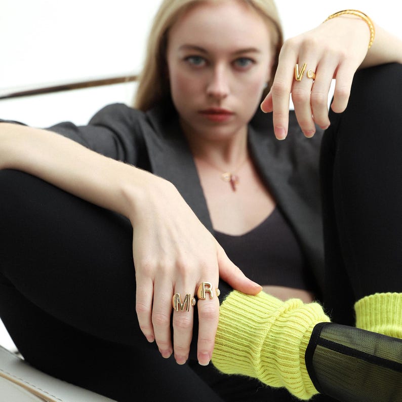 Woman wearing chunky gold rings with a sleek design, styled with gold hoop earrings and a matching bracelet.
