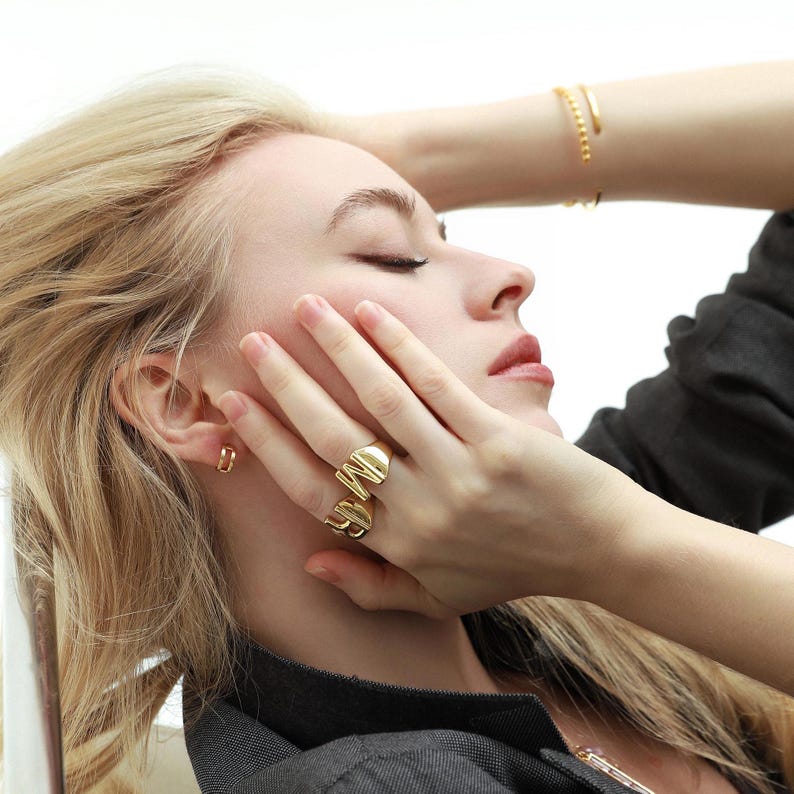 Woman wearing chunky gold rings with a sleek design, styled with gold hoop earrings and a matching bracelet.