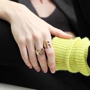 Woman wearing chunky gold rings with a sleek design, styled with gold hoop earrings and a matching bracelet.