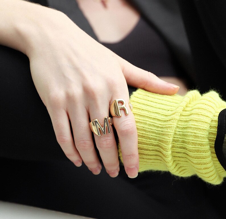 Woman wearing chunky gold rings with a sleek design, styled with gold hoop earrings and a matching bracelet.