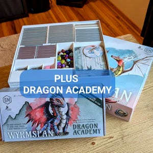 May include: A board game set with multiple boxes and components. The boxes feature dragon illustrations and the text "Dragon Academy" and "Wyrmspan". The set includes cards, game pieces, and a storage container with compartments. The text "PLUS" is also visible.