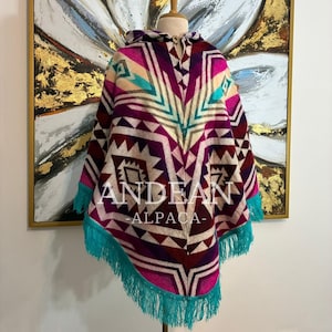 Peut inclure: Un poncho à capuche arborant un motif géométrique dans des tons magenta, violet profond, crème et turquoise. Le vêtement présente une fermeture à bouton en bois unique au niveau du col et une longue frange turquoise sur l'ourlet inférieur.