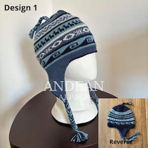 May include: A blue knit earflap hat featuring a multi-coloured geometric pattern with stylised animal silhouettes, a braided top tassel, and two braided side tassels. The hat displays the text Design 1 and Andean Alpaca.