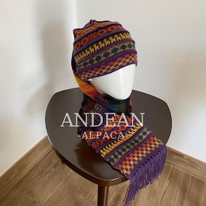 May include: A purple knit beanie and matching scarf set featuring a multi-colored geometric pattern with orange, yellow, and green accents. The scarf includes fringe at the ends. The text "ANDEAN ALPACA" is printed in white across the center.